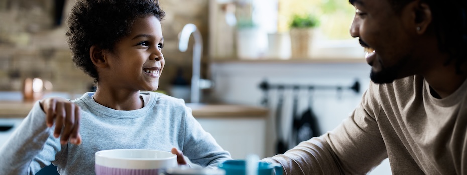 A parent and child smile at each other while sitting at the kitchen table.