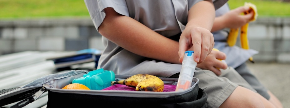 A child takes an epinephrine auto-injector out of a lunch bag filled with food.