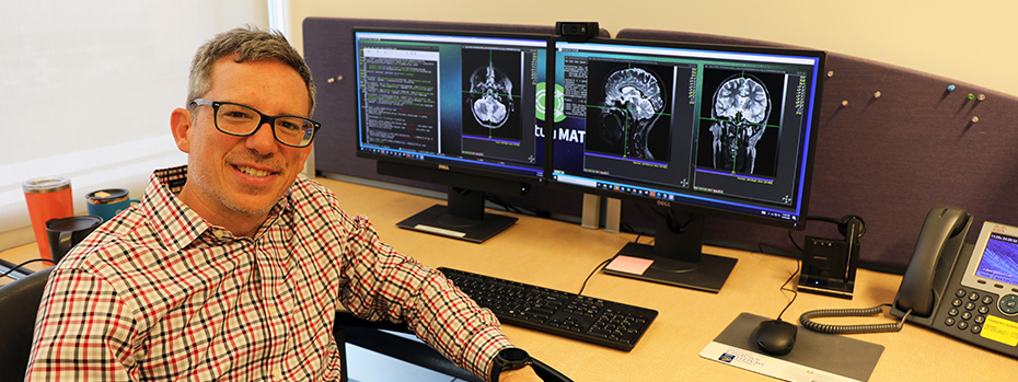 Juan Piantino, an 博彩网站 pediatric neurologist, sits in front of two computer monitors showing images of brains.