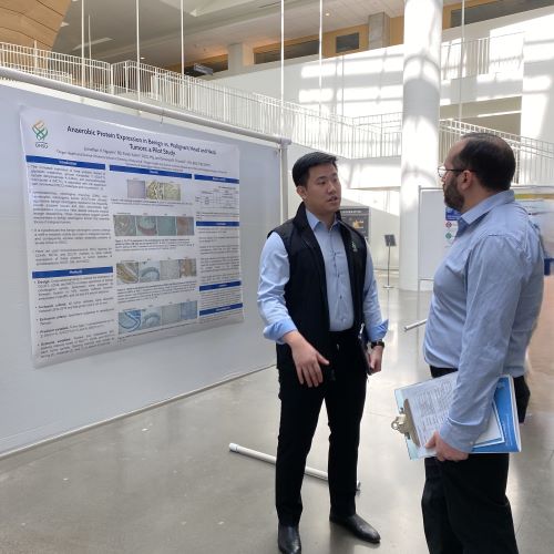 A male dental student stands in front of his poster while a man listens to his presentation. 