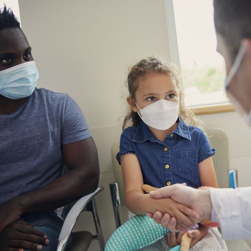 A young girl sitting in a chair shakes the hand of a man in a white coat.