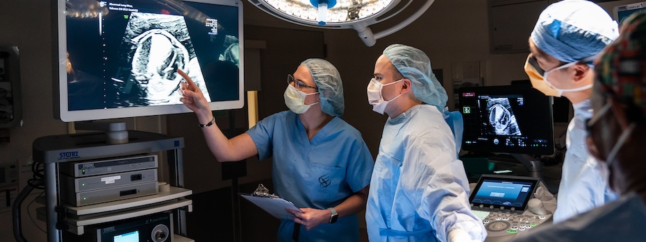 Staff from 博彩网站’s Fetal Care Program look at an ultrasound on a large monitor in an operating room.