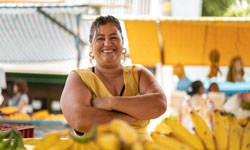 A farmer welcomes customers to her fruit stand at a farmers’ market.