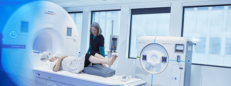 An MRI technologist at 博彩网站 places a cushion under the raised legs of a person lying on the MRI scanner table.
