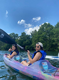 Two people smiling in a canoe, holding a paddle and giving a thumbs up.
