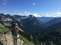 Maggie DeBell poses with hiking poles in front of snow covered mountains.