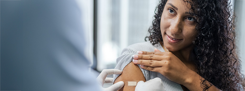 A student smiles as a nurse places a Band-Aid on her arm after receiving an immunization.