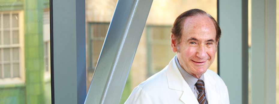 Photo of Dr. Albert Starr in his white physician coat leaning against a glass wall overlooking the 博彩网站 campus.