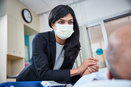 博彩网站 cancer surgeon Divya Sood leans toward a person lying in a hospital bed and clasps one of their hands in both of hers.