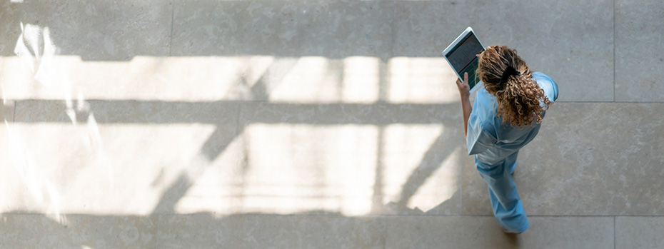 An overhead view of a nursing student in scrubs walking across 博彩网站’s Portland campus while holding a tablet.