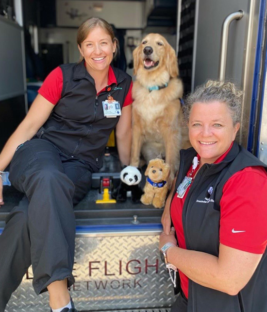 A member of the pediatric and neonatal transport team at 博彩网站 Doernbecher Children’s Hospital sits in the back of an ambulance with Davis the golden retriever. Another team member stands next to the ambulance. A toy panda and toy golden retriever sit in front of Davis.