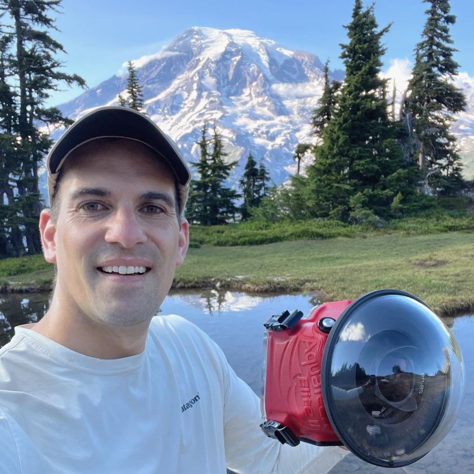 Chris Liedle with Mount Rainier behind him and holding a camera