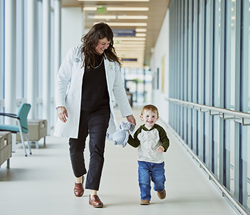 A doctor walks with a child patient down a hallway in a hospital.