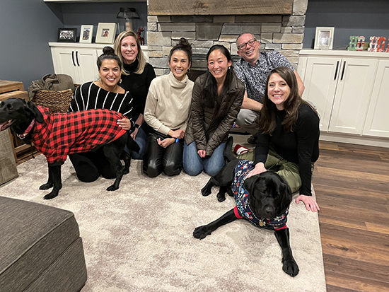 Six members of the Piantino Lab and two dogs sit together in front of a fireplace.
