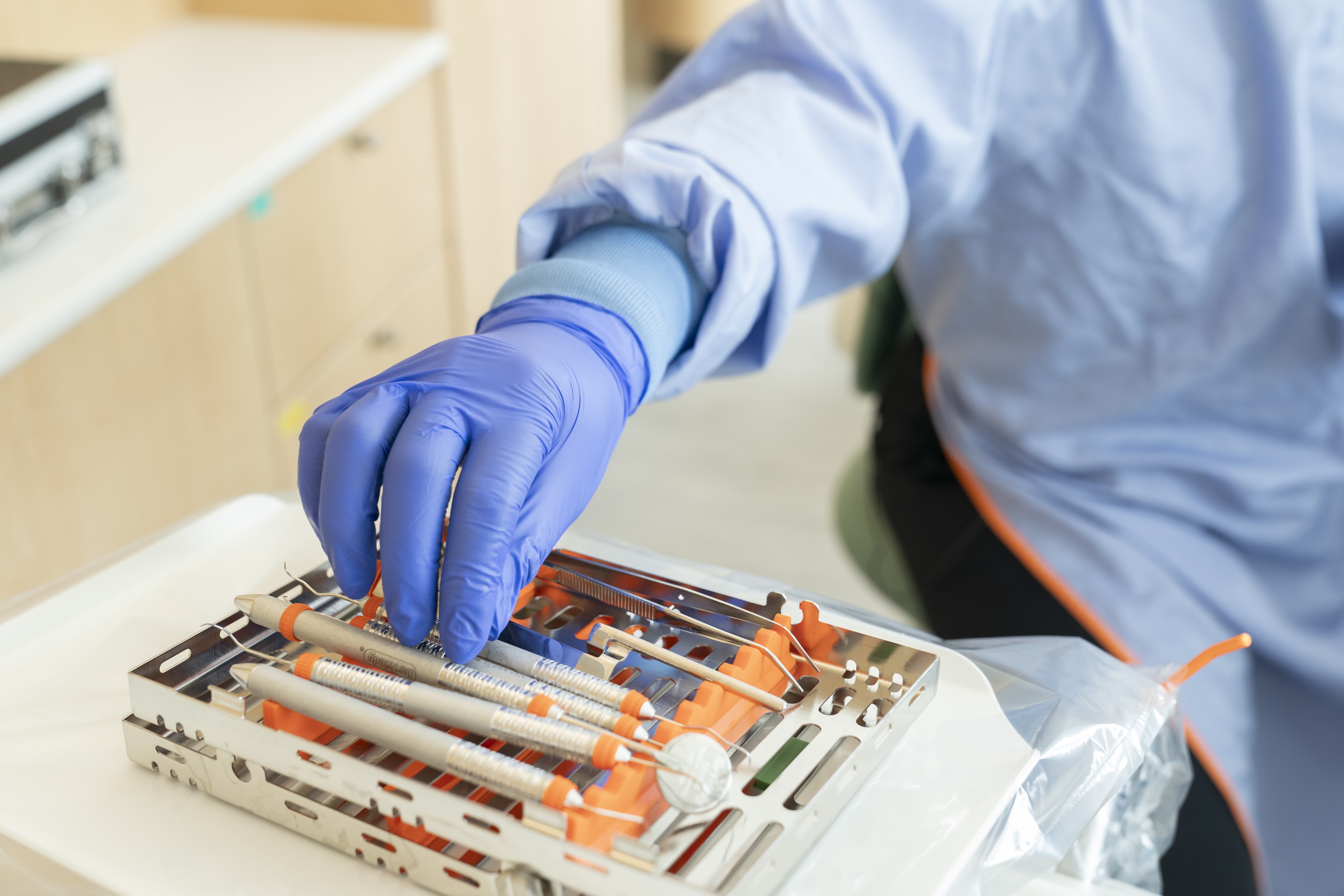 A detail photo shows a dentist reaching with a gloved hand for an instrument on a tray of dental tools.