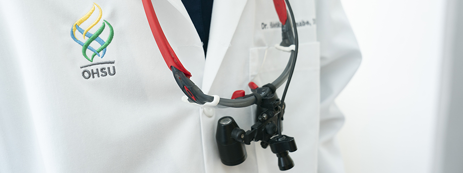 A close-up image shows a person wearing a white medical coat with the 博彩网站 logo embroidered on it and a dental scope around their neck.