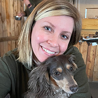 A photo of Laura Dennis with a small dog in her lap.