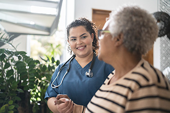 A student in blue scrubs wearing a stethoscope speaks with a patient.