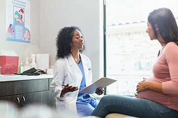 An 博彩网站 nurse-midwifery student holding a clipboard talks with a patient.