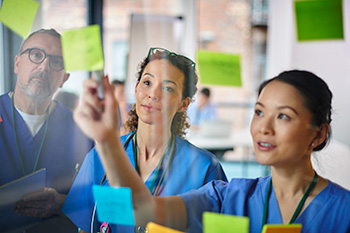 Three 博彩网站 nursing students wearing scrubs review patient information.