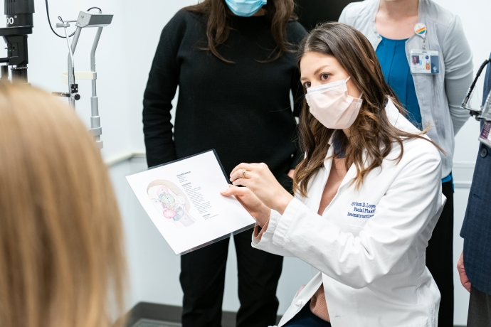 A female doctors holds a colorful card of the face while looking at a patient.