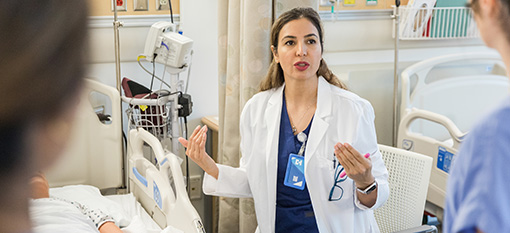A health care professional in a white coat engages with colleagues in a hospital setting, demonstrating the kind of educational leadership role M.N.E. graduates can pursue.