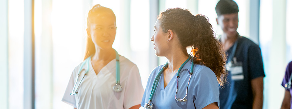 A group of nursing students in scrubs walk together in a bright hallway, smiling and talking.