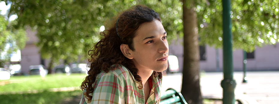 A transgender woman sits on a park bench on a sunny day