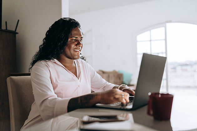 A transgender woman works on a laptop at home.