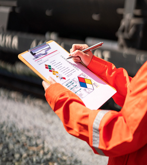 Action of an engineer is checking on chemical hazardous material checklist form with background of train freight tanker for crude oil or chemical cargo. Industrial safety working scene.