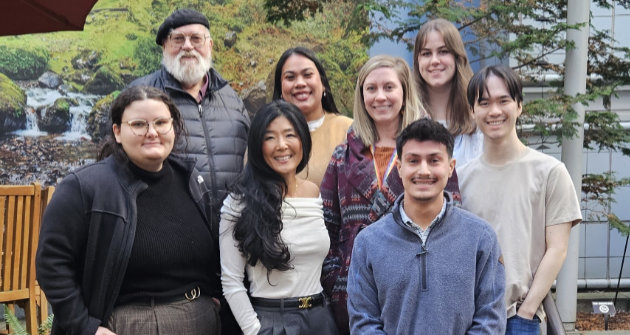 Nine members of the 博彩网站 BRAIN Lab pose together in front of the Portland VA, building 1.