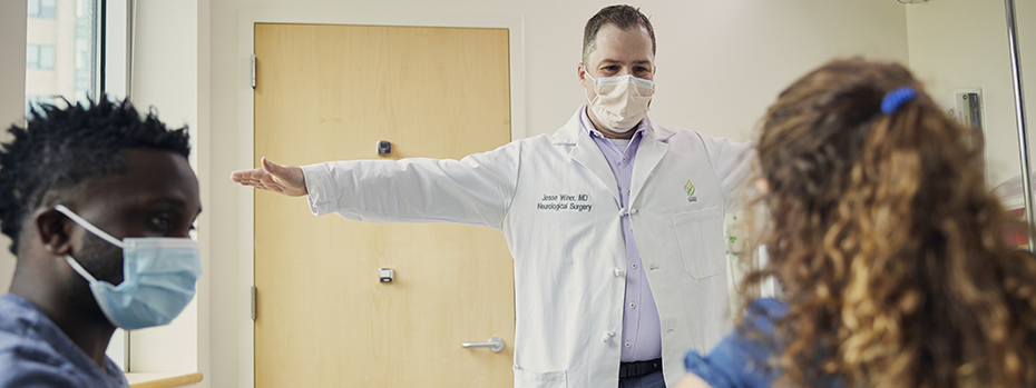 Dr. Winer holds his arms out to his sides. A young female patient does too while her parent watches.