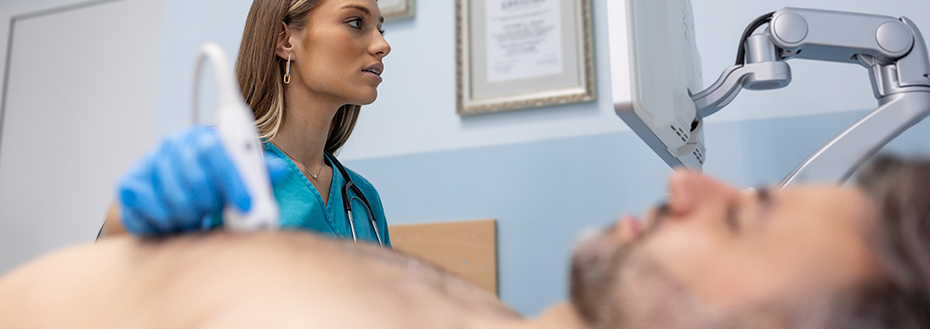 : A cardiac imaging specialist performs an echocardiogram on a male patient who is lying down in a doctor’s office.