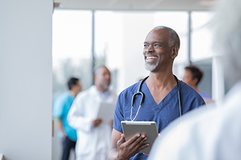 A student wearing blue scrubs and a stethoscope smiles and looks off into the distance.
