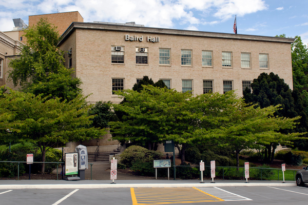 Brick building with windows and trees and a parking lot in front of it Brick building with windows and trees and a parking lot in front of it
