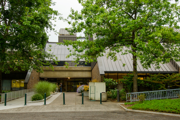 Building with sloped roof with trees in front of it Building with sloped roof with trees in front of it